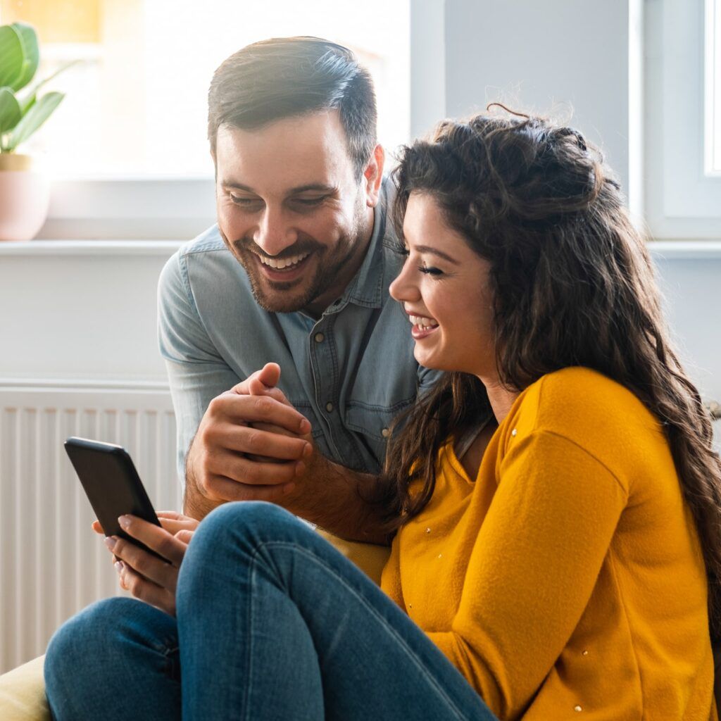 Cheerful couple using mobile phone at home stock photo