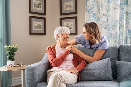 Smiling adult daughter embracing old mother sitting on sofa