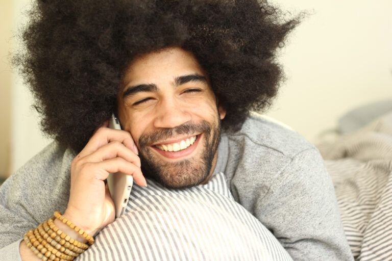 Man in a bedroom smiling while talkin on phone call