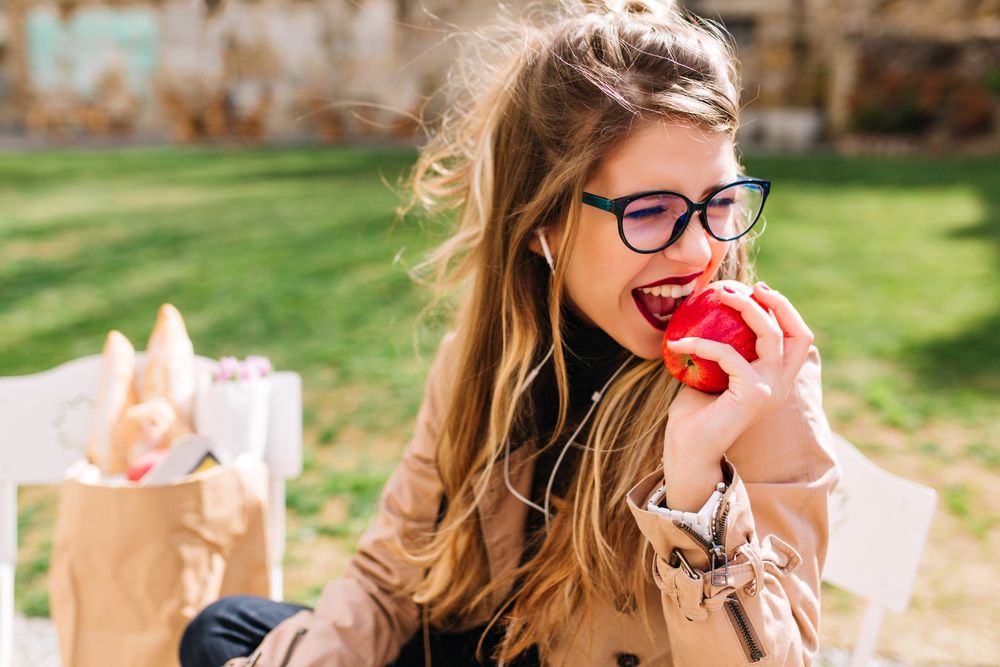 Girl with appetite bites off red apple sitting in the park