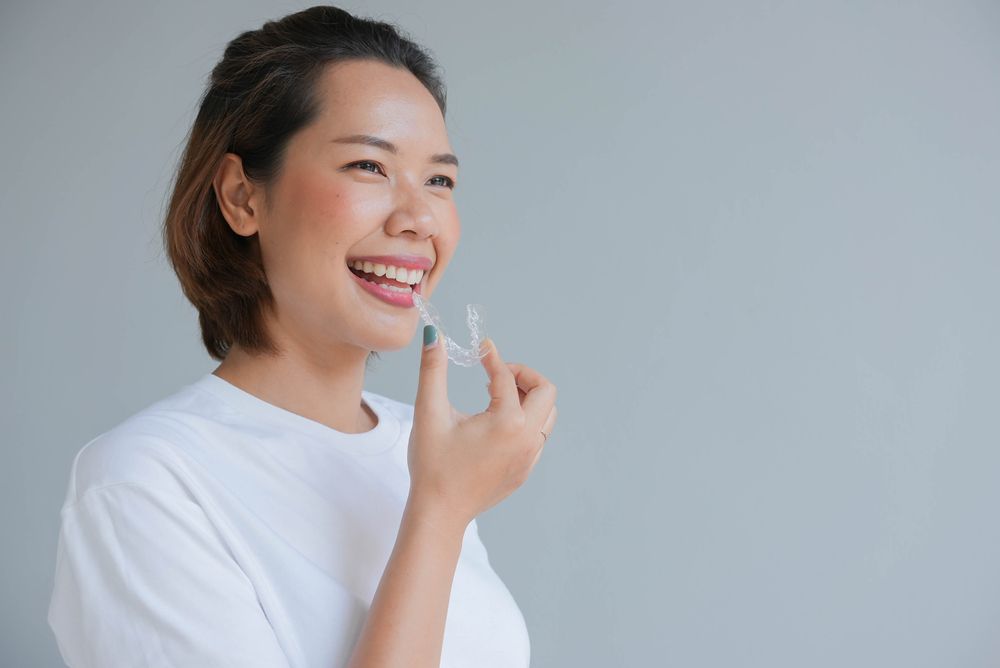 Young beautiful woman smiling with hand holding dental aligner retainer