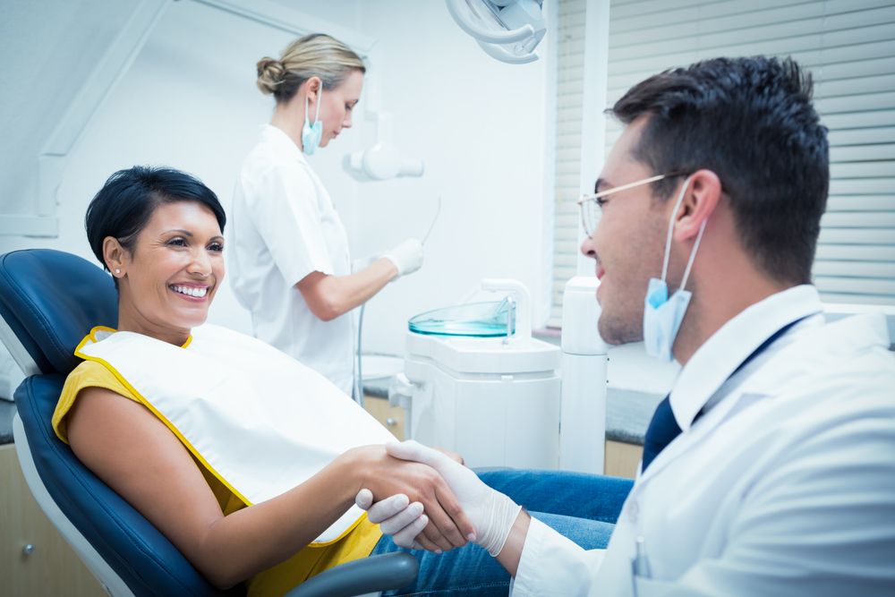 Male dentist shaking hands with woman in the dentists chair