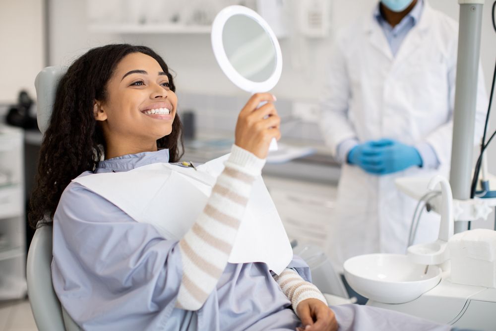 Happy female patient looking at mirror after dental treatment in clinic