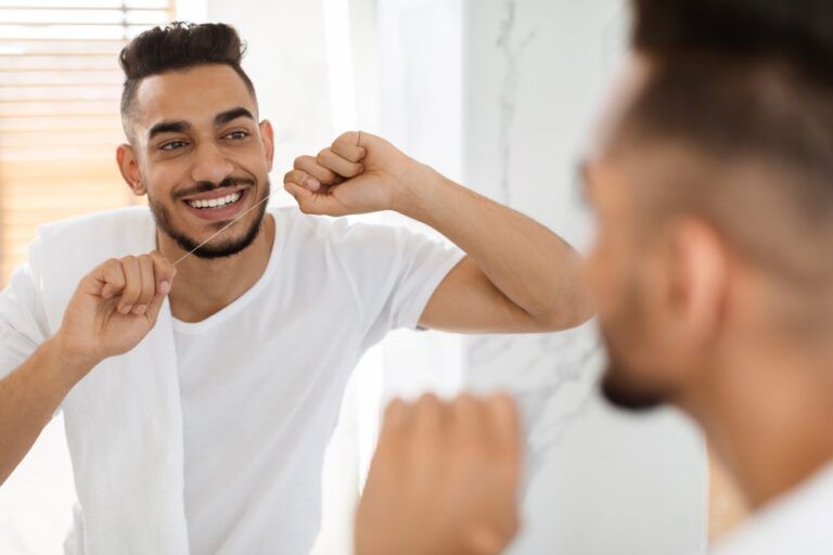 Smiling man Using Dental Floss While Standing Near Mirror In Bathroom