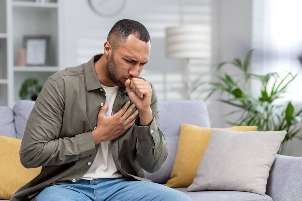 Young man sitting on the couch at home and coughing