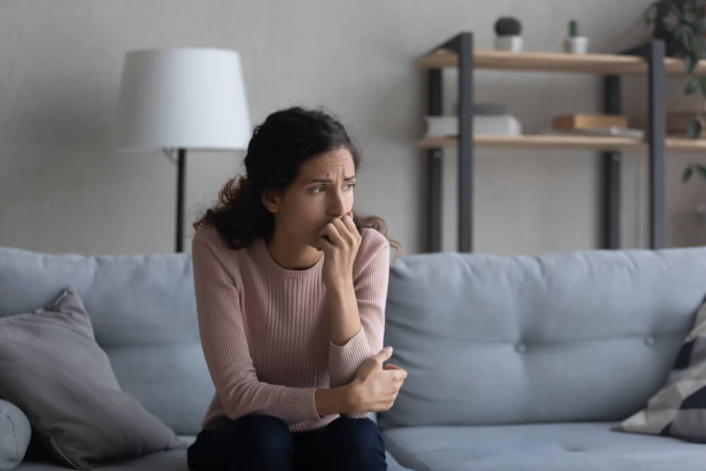 Sad young woman sit on couch at home