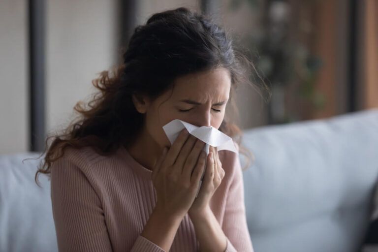 Sick young woman sit indoors holding tissue blowing running nose