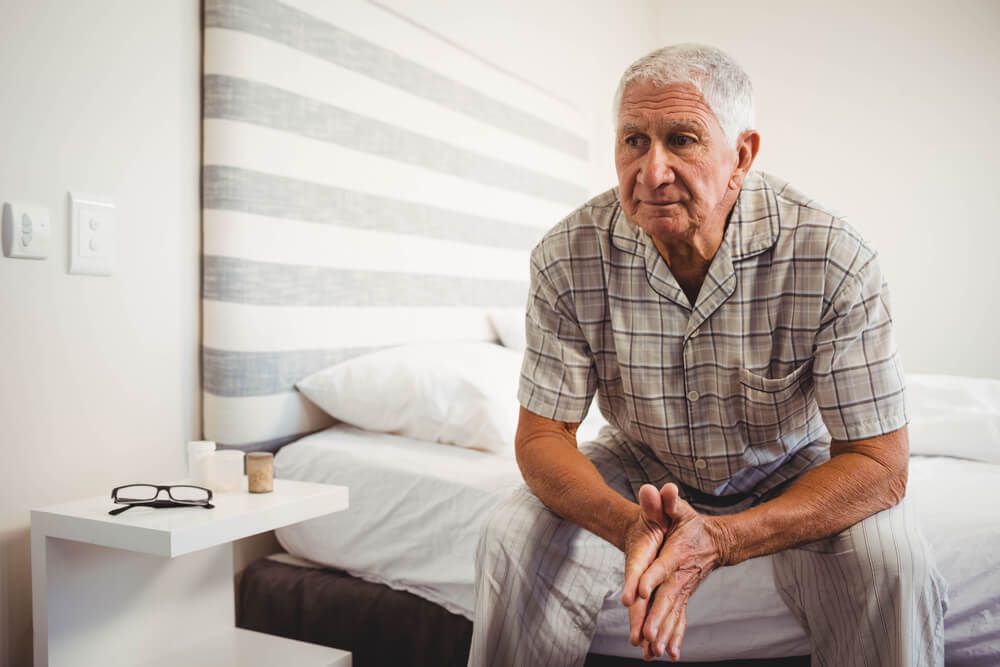 Senior man sitting on bed in bedroom