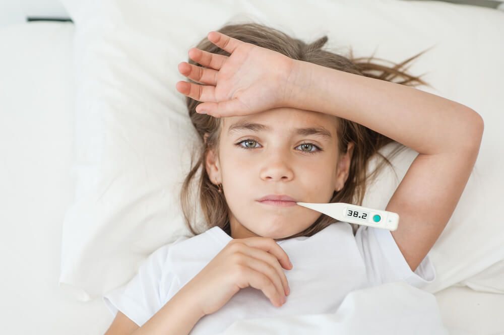 sick girl lying in bed with a thermometer in mouth