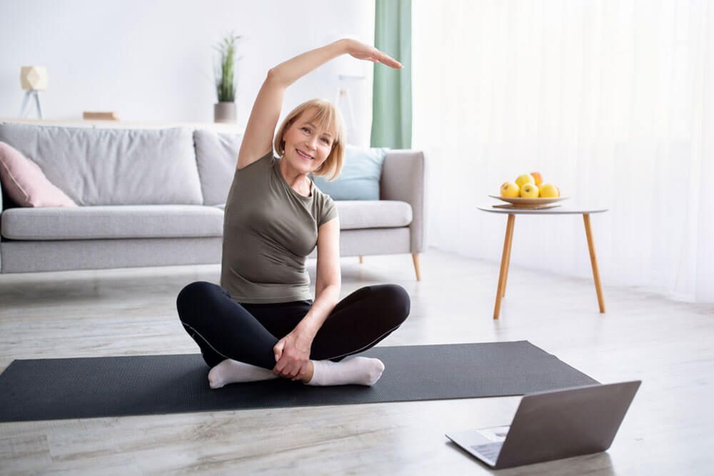 Athletic senior woman doing yoga in front of laptop