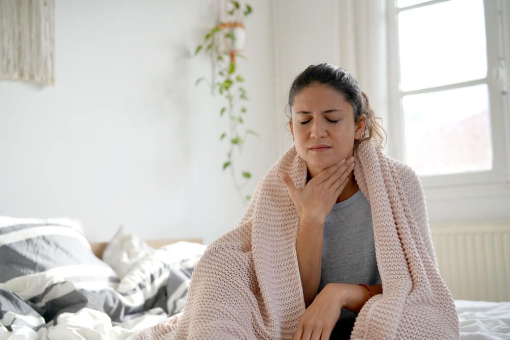 Attractive woman sitting on bed with sore throat