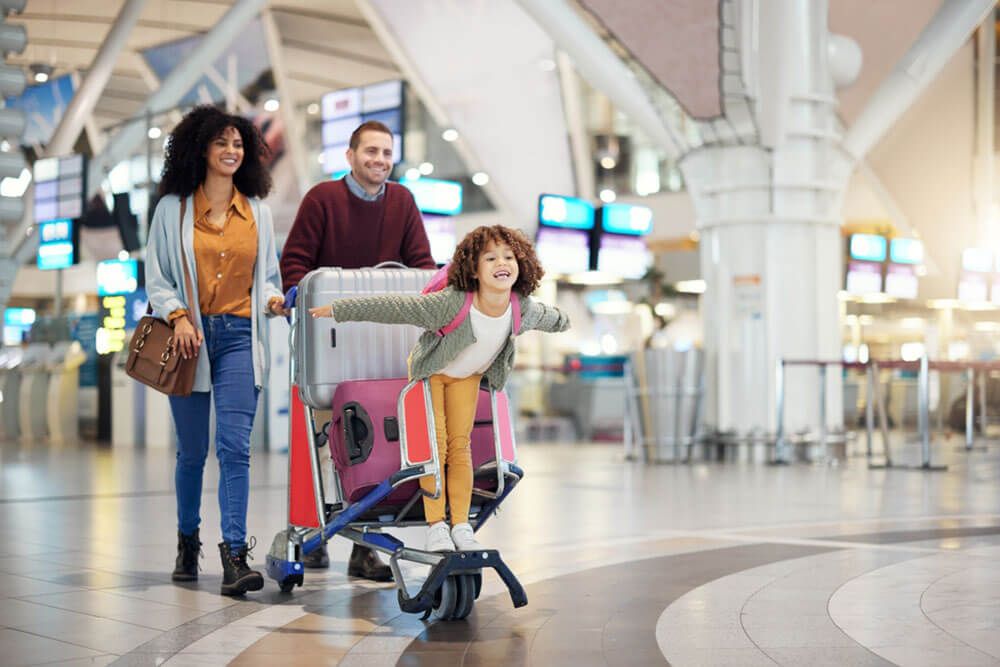 Family and child excited for flight with suitcase trolley on holiday