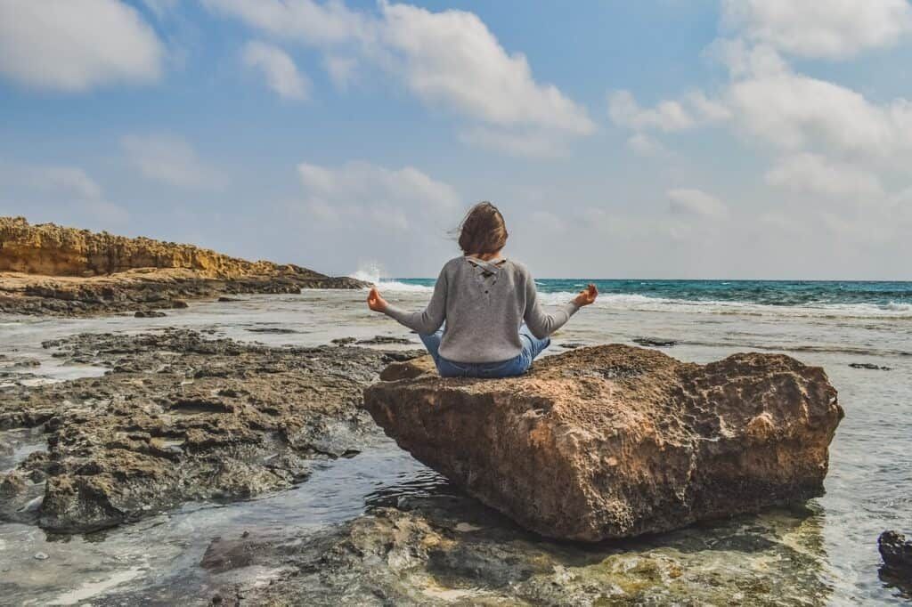 Girl practicing yoga on the seashore in front of a landscape
