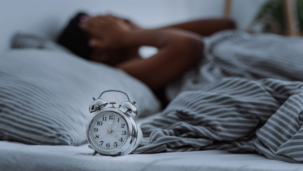 woman suffering from insomnia lying in bed without sleep with alarm clocks