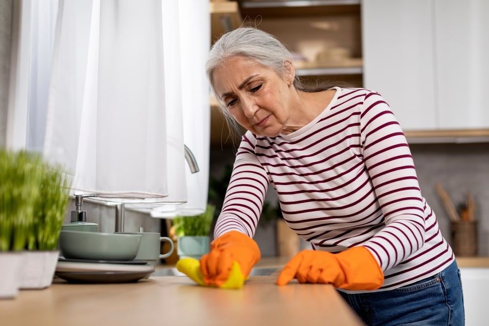 Tired Senior Woman Cleaning Table In Kitchen