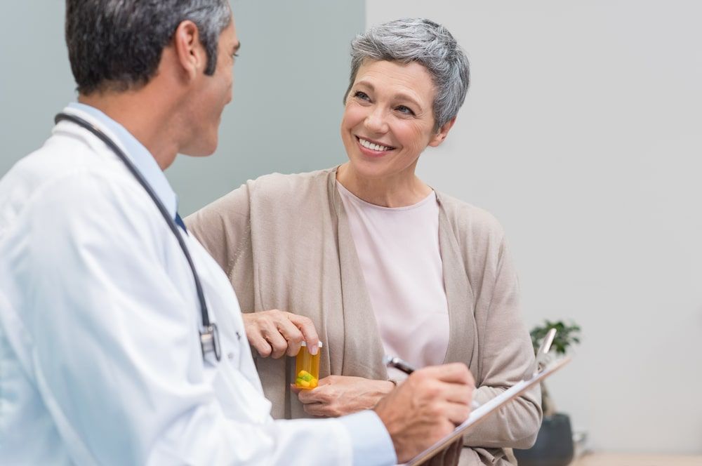 Senior doctor in conversation with senior woman holding medicine box