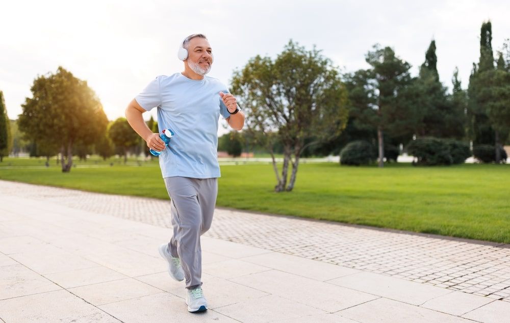 happy senior man in sportswear jogging outside in city park