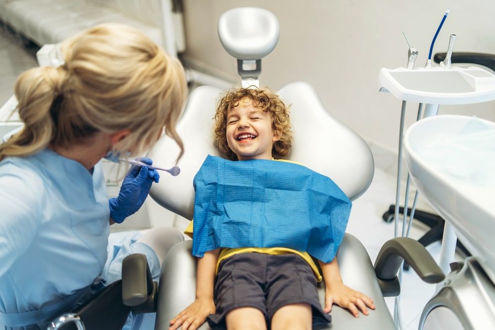 Cute young boy visiting dentist, having his teeth checked by female dentist