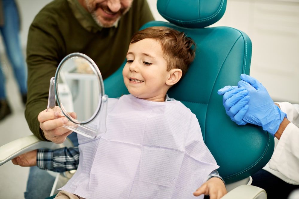 Smiling little boy looking at his teeth in mirror