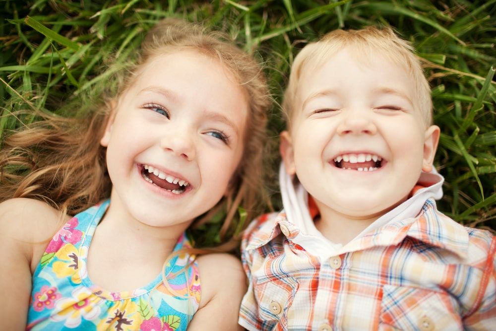 Two happy smiling kids lying on green grass