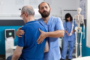 Orthopedic nurse stretching spinal cord and shoulder of elder patient with injury for physiotherapy