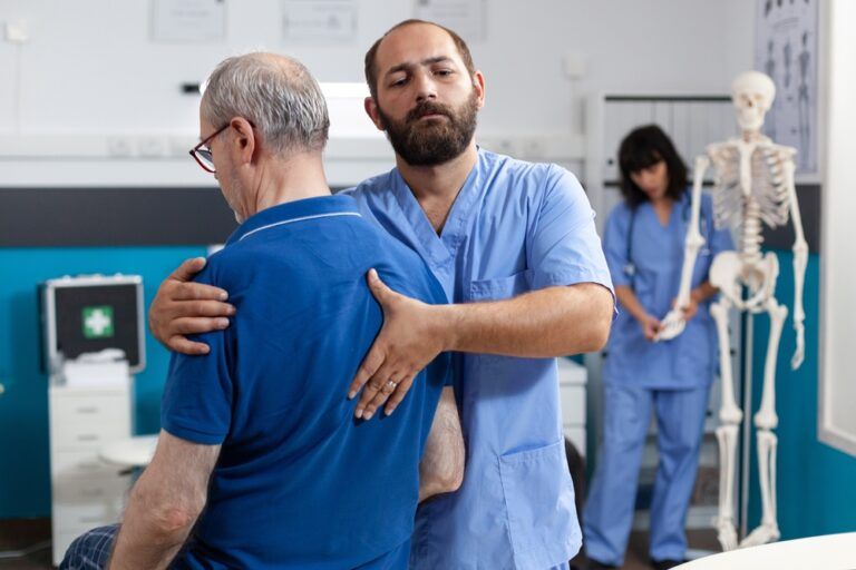 Orthopedic nurse stretching spinal cord and shoulder of elder patient with injury for physiotherapy