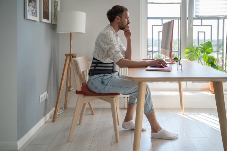 Focused male freelancer wearing lumbar brace sitting at table using computer