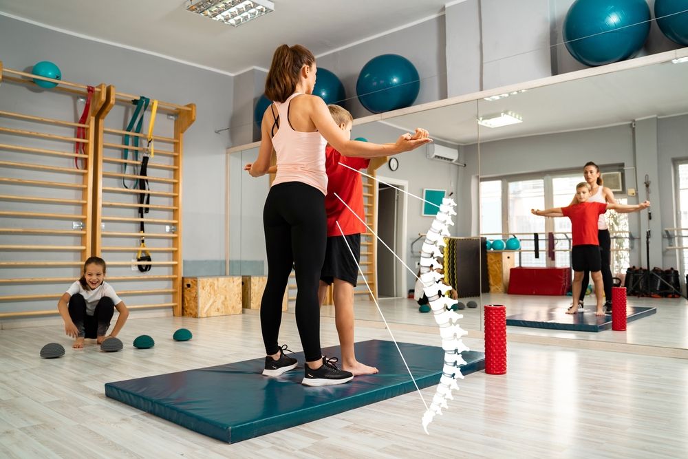 Physical therapist checking health of boys spine, indoors in gym. Posture, kids and spine health