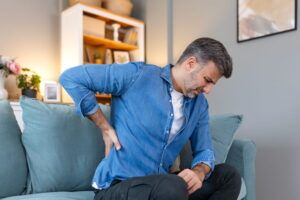 Handsome man touching his back, suffering from backpain, sciatica, sedentary lifestyle concept. Spine health problems. Healthcare, insurance