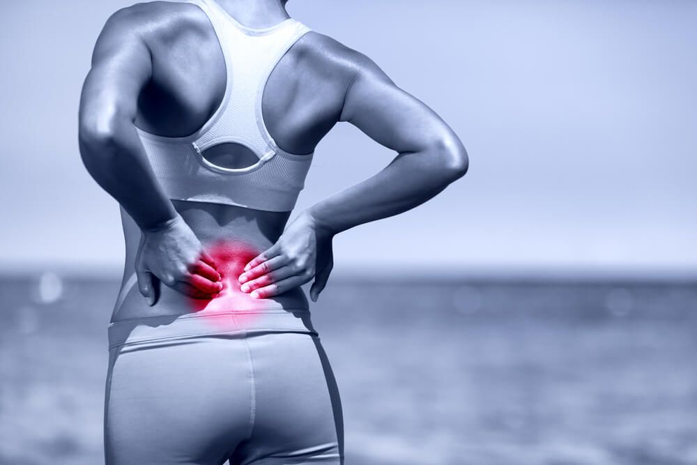 Athletic running woman with back injury in sportswear rubbing lower back
