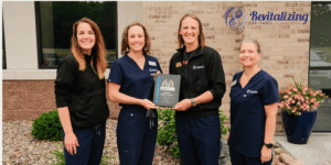 The Revitalizing Health & Hormones team poses together holding their BusinessRate award recognizing the clinic as the #1 Healthcare Clinic in Eau Claire County for excellence in patient care, reputation, and patient satisfaction.