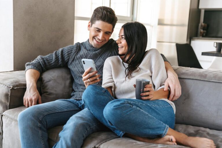 Happy young couple sitting on a couch at home, drinking tea