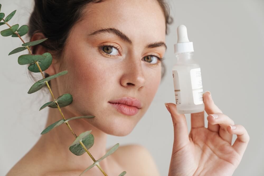 Half-naked brunette woman showing face serum