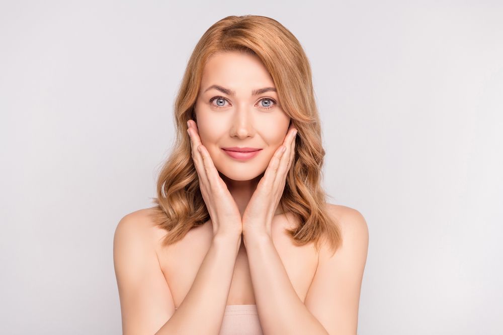 Portrait of attractive cute healthy woman washing face moisturizing isolated over grey pastel color background