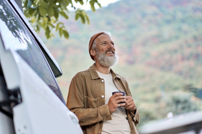 Active old happy hipster man standing near rv camper van on vacation