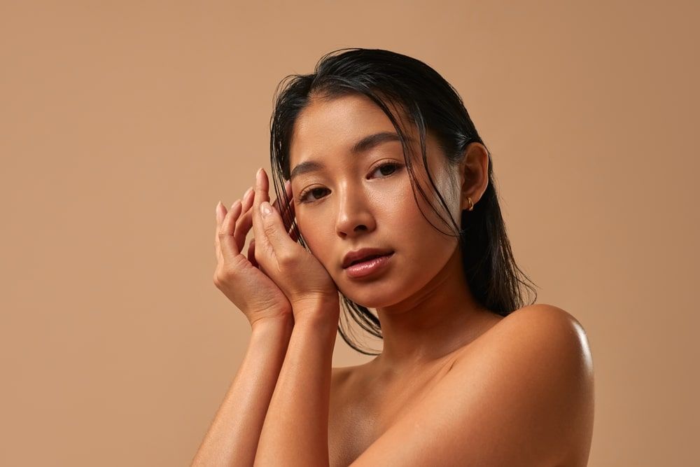 Asian woman with clear glowing skin posing isolated on beige background. The concept of skin care, cosmetology and spa treatments.
