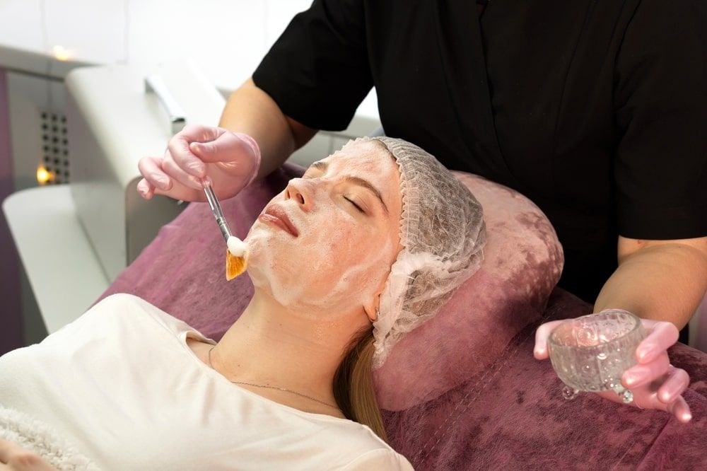 Esthetician applies fanbrush foamy mask to client’s chin. Facial beauty treatment. First stage of oxygen jet peeling