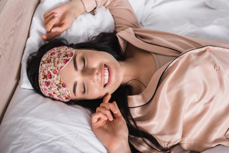 top view of smiling young brunette woman lying in bed in sleep mask