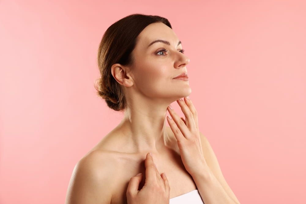 Woman touching her neck on pink background