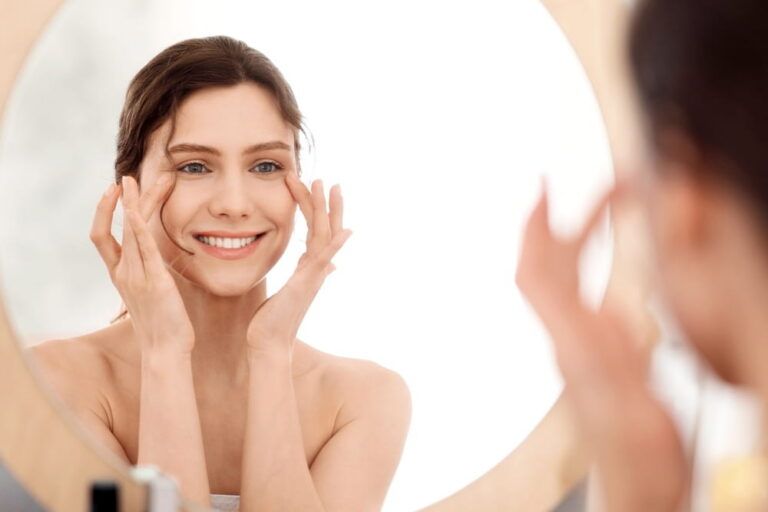 Eye care routine. Young woman massaging eye zone, looking at mirror, home interior