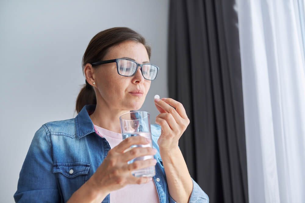 Mature middle-aged woman at home holding pill and glass of fresh water