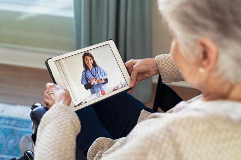 Back view of senior woman sitting in wheelchair making video call with her doctor