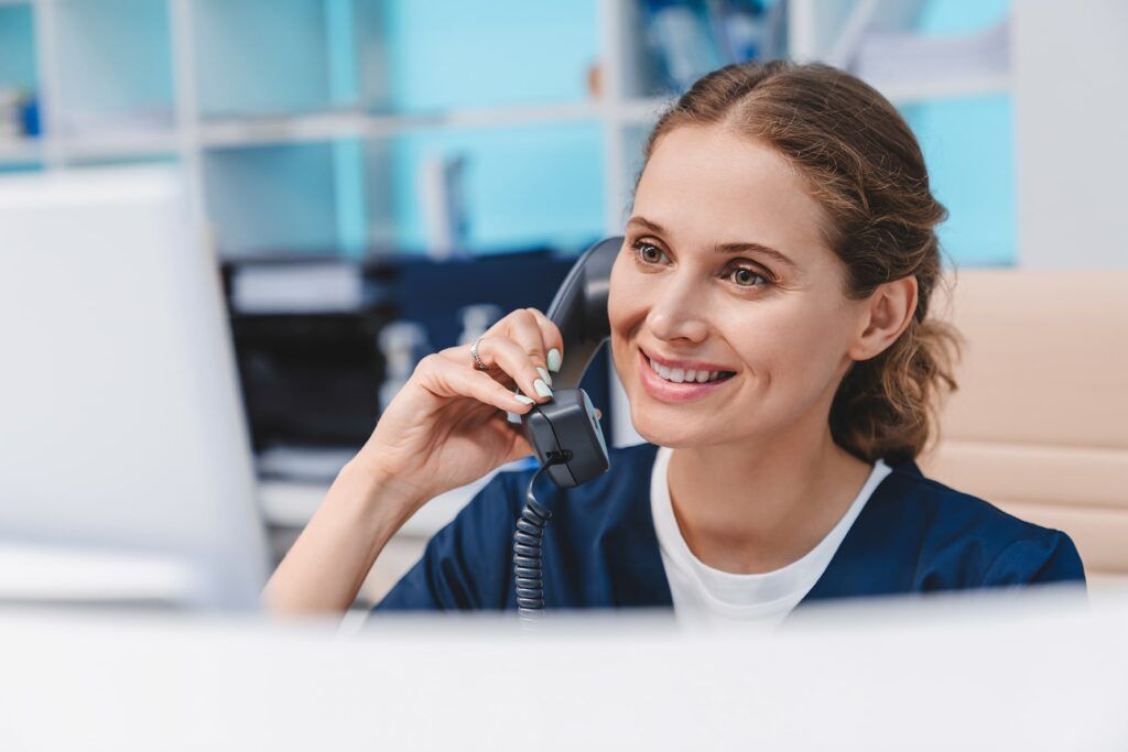 Young female doctor practitioner working at reception desk while answering phone calls and scheduling appointments