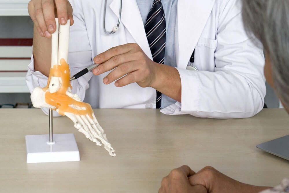 Orthopedic Surgeon in white gown and stethoscope pointing at human skeleton