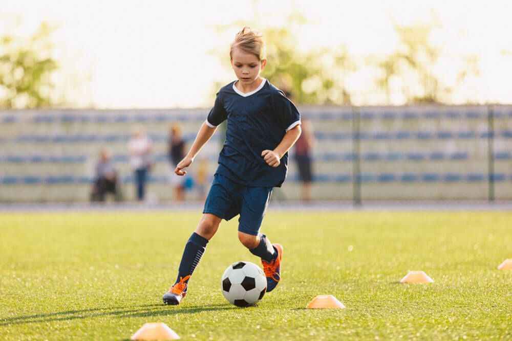 Young boy in blue soccer jersey uniform running after ball