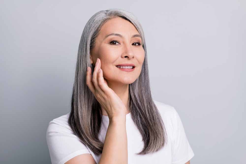 Senior woman with grey hair touching cheek wearing white t-shirt