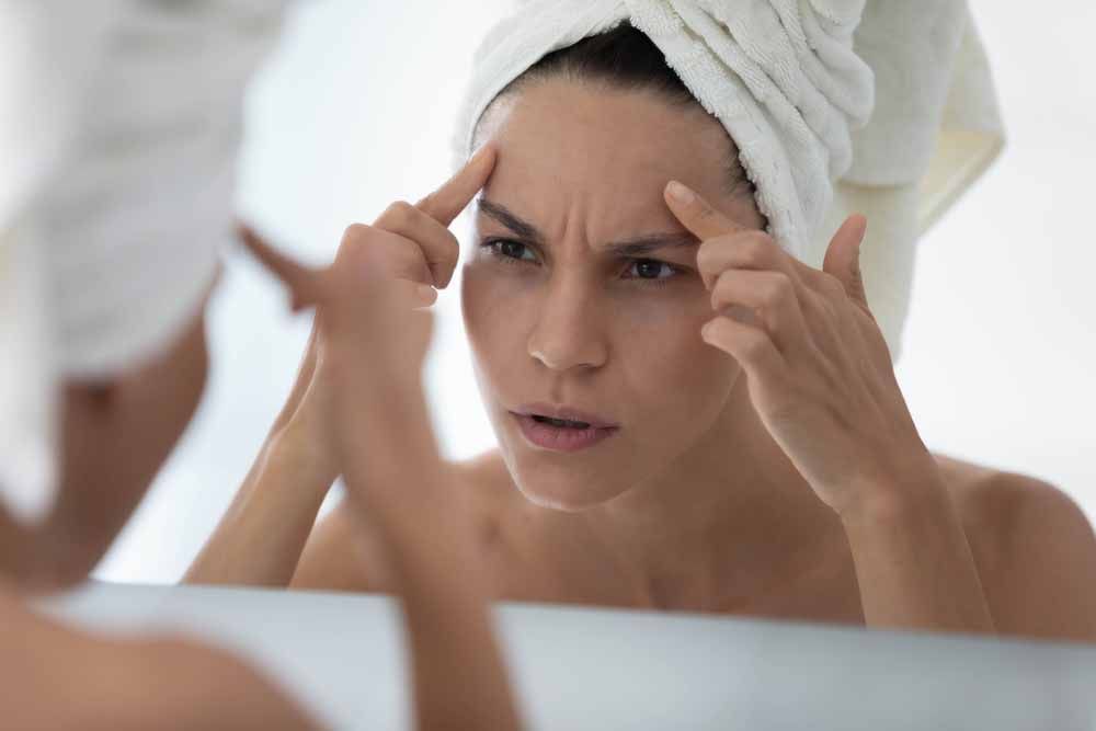 Worried young woman wrapped in towel looking in mirror in bathroom