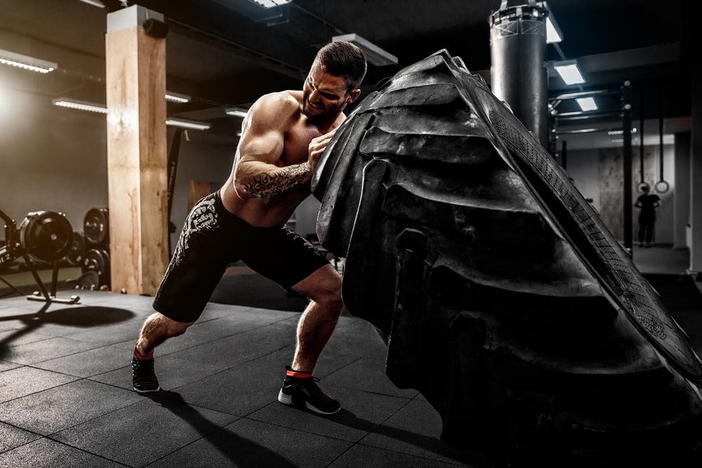 Shirtless man flipping heavy tire at gym