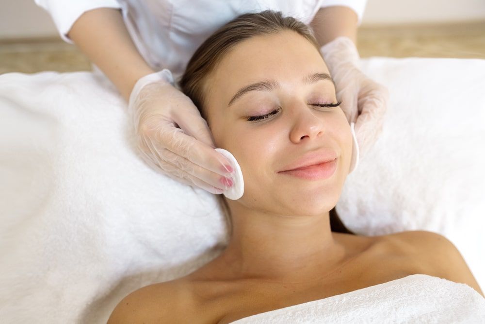 The beautician cleans the face from cosmetics to the patient before the procedure