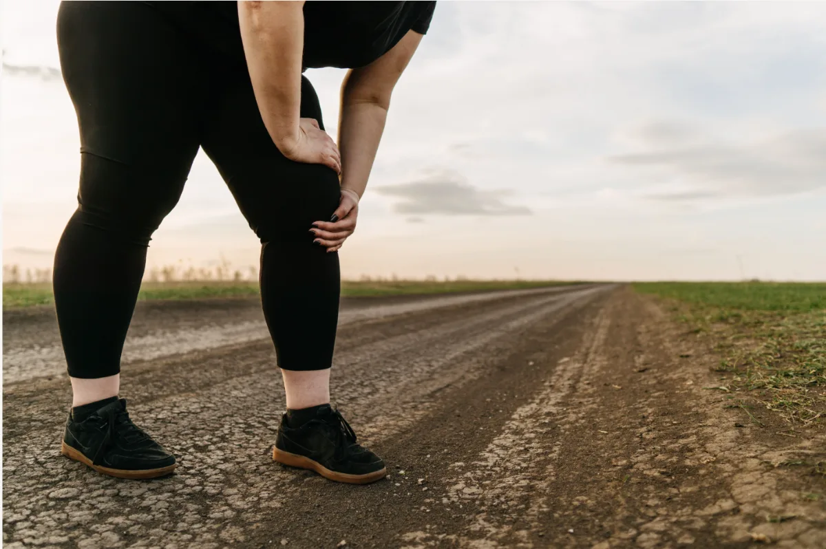 Person holding a painful knee while walking outdoors